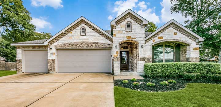 Brick and stone Falcon House with two garages, landscaped lawn, and vibrant green bushes in Schertz, TX available through TDY Haven Crash Pad